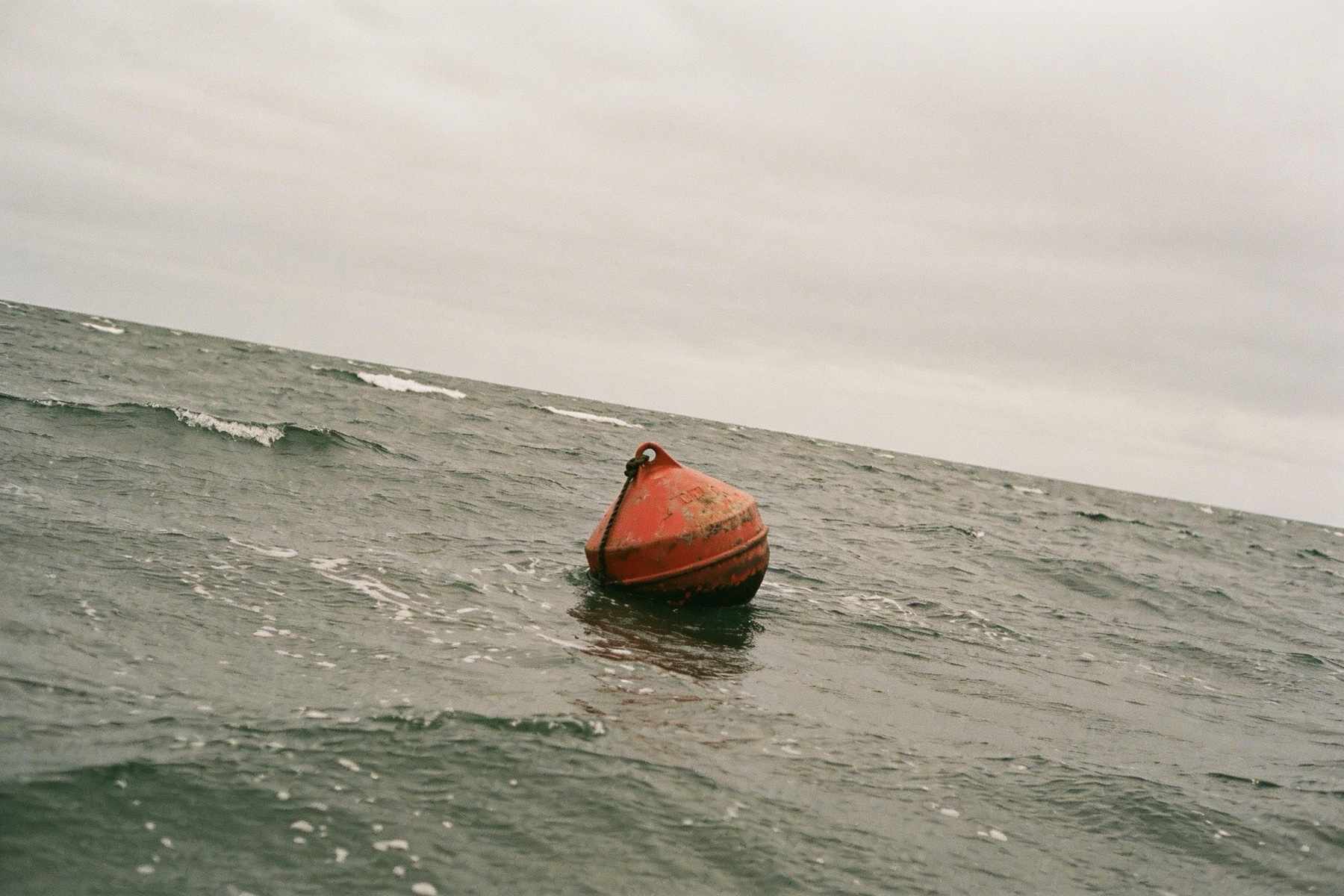 A faded orange mooring buoy riding choppy grey-green water under an overcast sky
